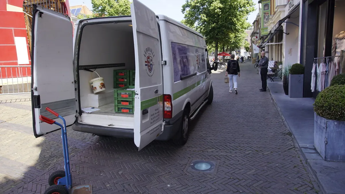 Witte bezorgbus met open laadruimte en steekwagen in een Nederlandse straat
