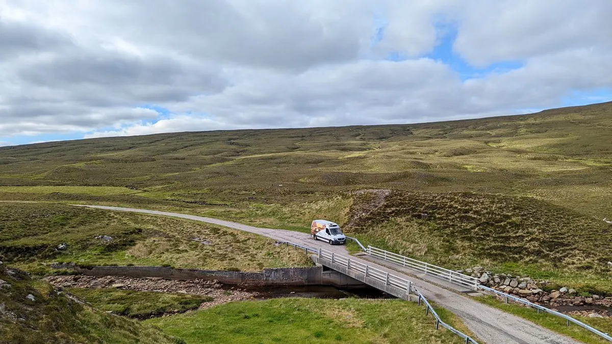 Witte bestelbus onderweg over een brug in een groen landschap